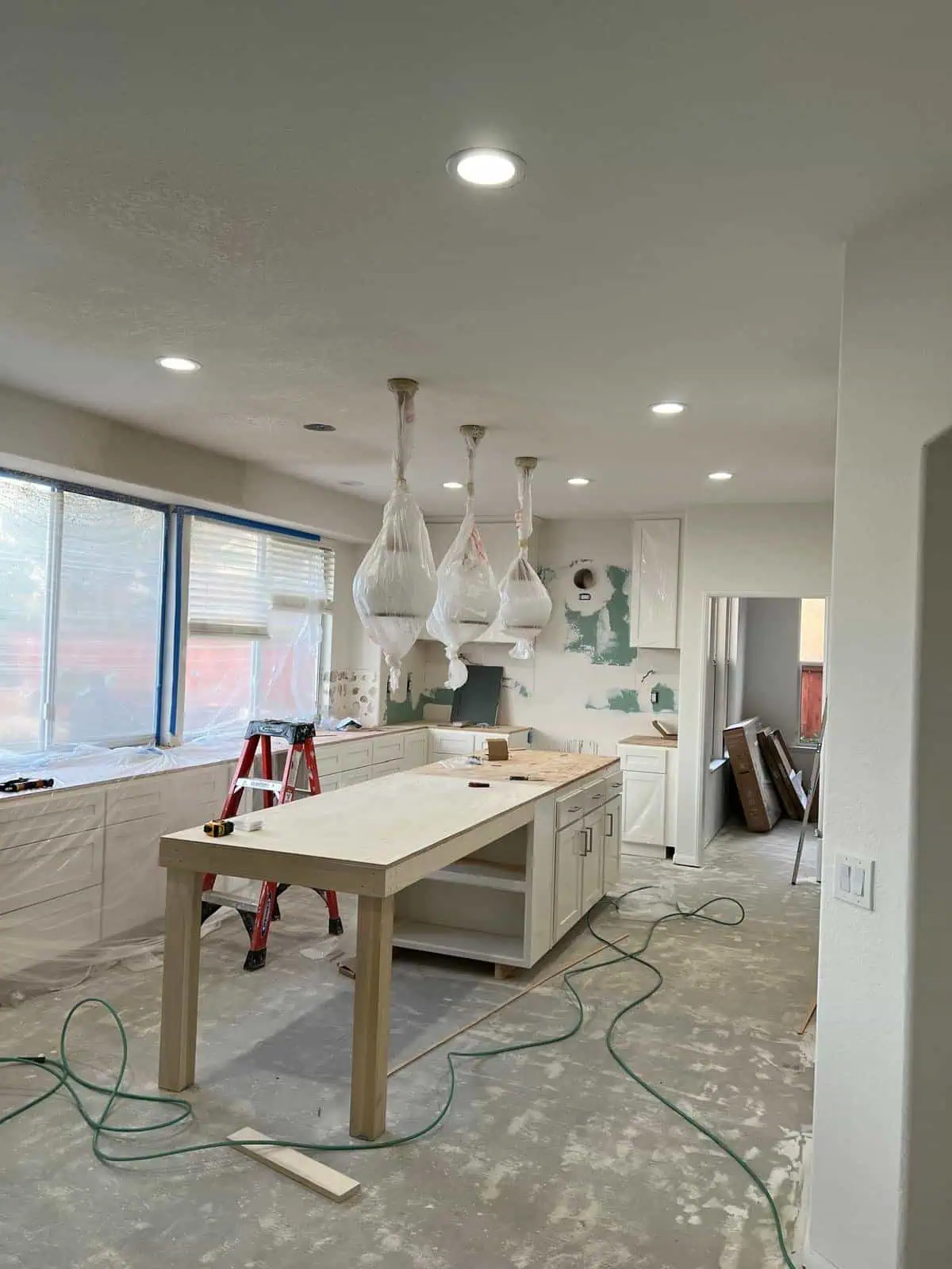 Newly renovated kitchen with hanging light fixtures and large windows, under construction.