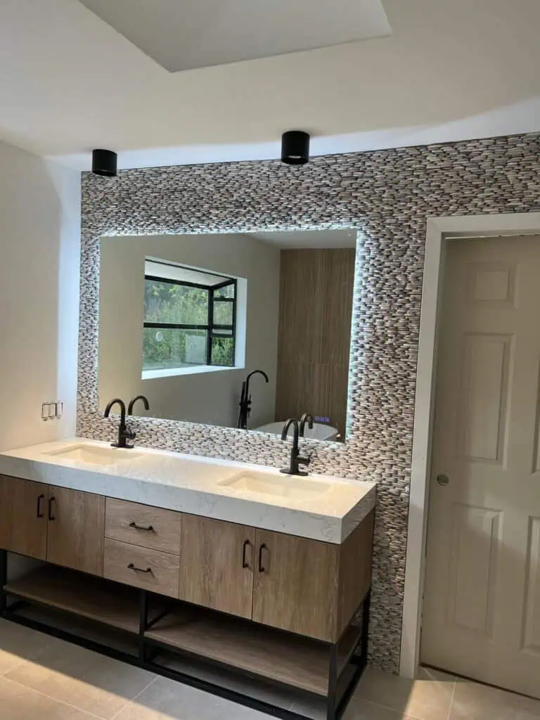 Bright modern bathroom vanity with dual sinks, stylish mosaic tile accent wall, and large mirror for.
