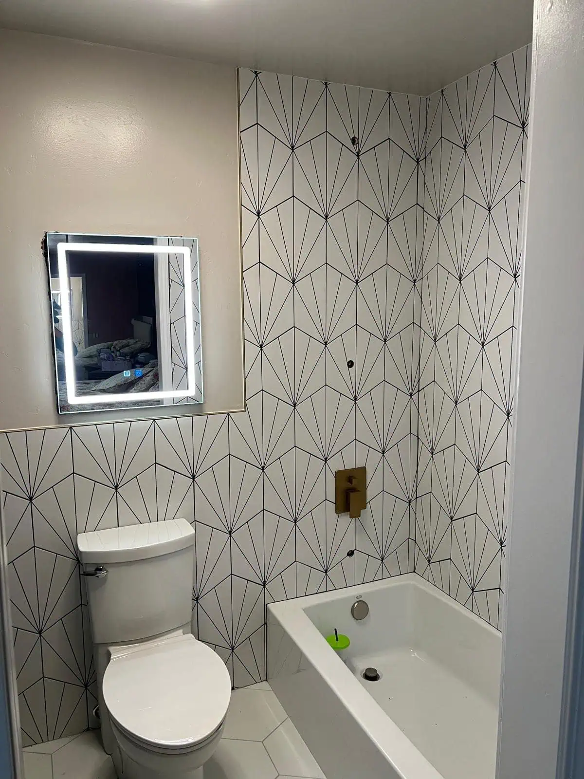 Modern bathroom with geometric tile wall, toilet, and bathtub.