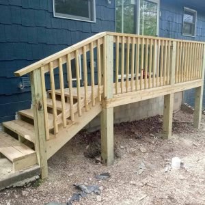 Newly built wooden deck with railing attached to a blue house exterior.