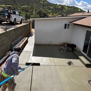 Newly poured concrete patio with workers finishing surface in a residential backyard.